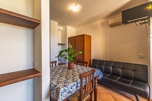 Un coin repas avec une table recouverte d’une nappe à motifs floraux, une plante en pot et un canapé en cuir noir.