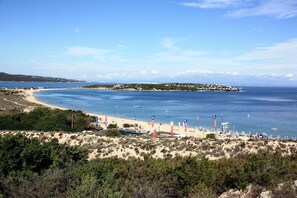 Une plage côtière avec un rivage sablonneux, une mer bleue et limpide, et une île qui se profile à l’horizon.