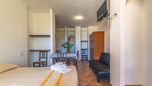 Een hotelkamer met een bed, een eettafel met stoelen, een bank en een aan de muur bevestigde televisie.