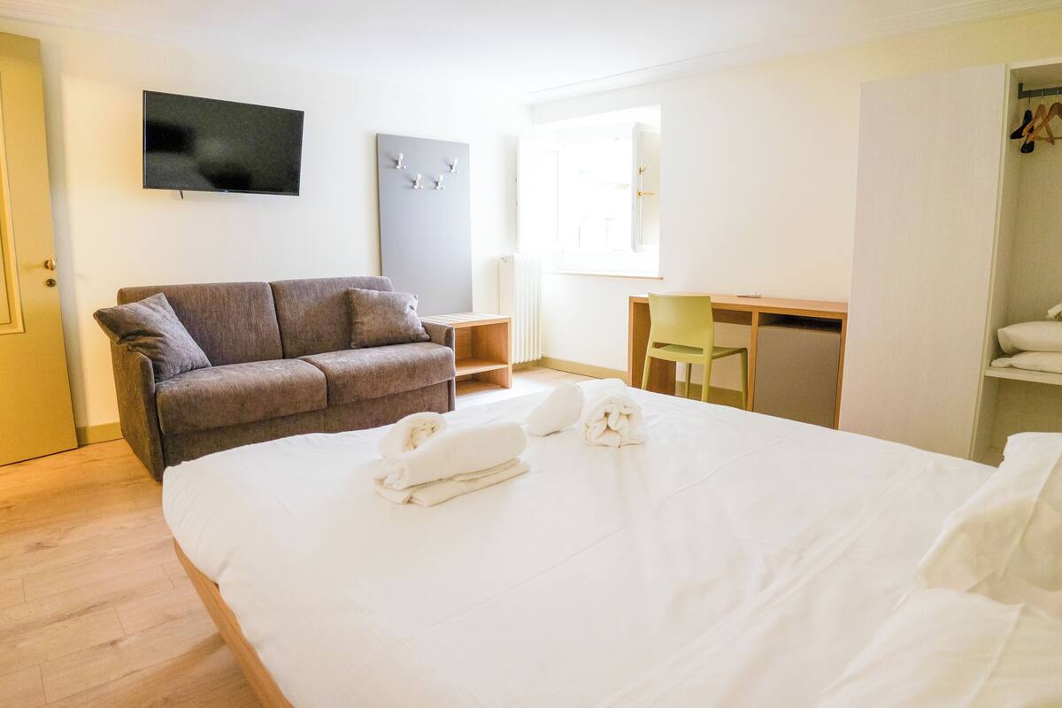 A hotel room with a large bed, a sofa, a desk, and a TV on the wall.
