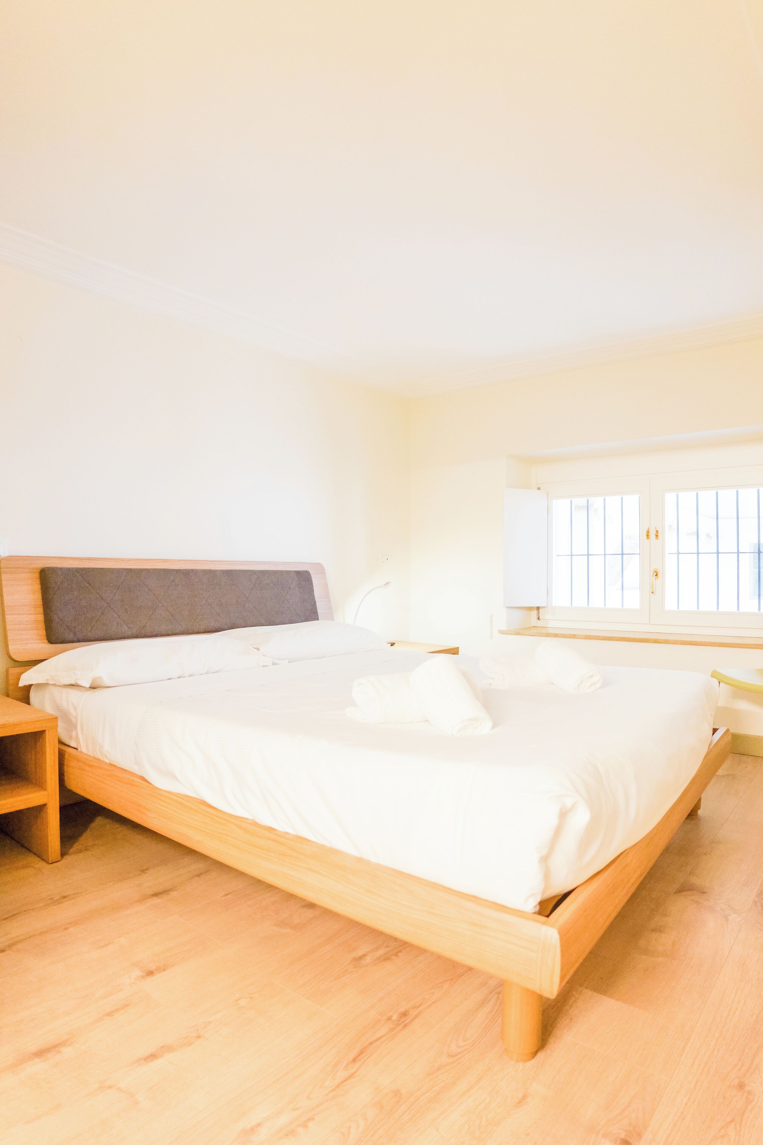 Quarto com cama de madeira, mesa de cabeceira e janela com persianas.