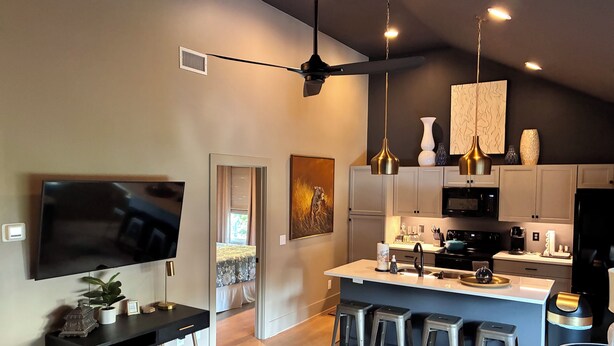 A modern kitchen with a central island, bar stools, a flat-screen TV, and pendant lighting.