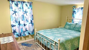 A bedroom with a bed, a nightstand, a wooden desk, and a patterned rug.