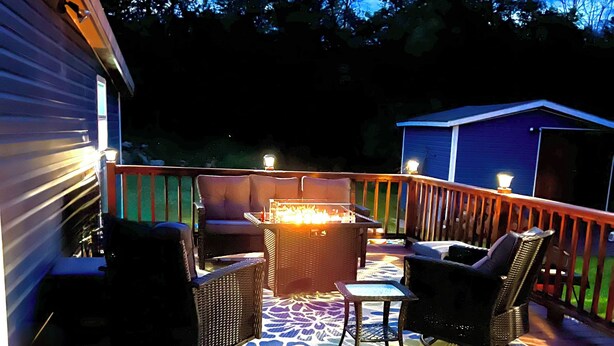 A wooden deck with outdoor furniture, a fire pit, and a view of the surrounding trees and sky.