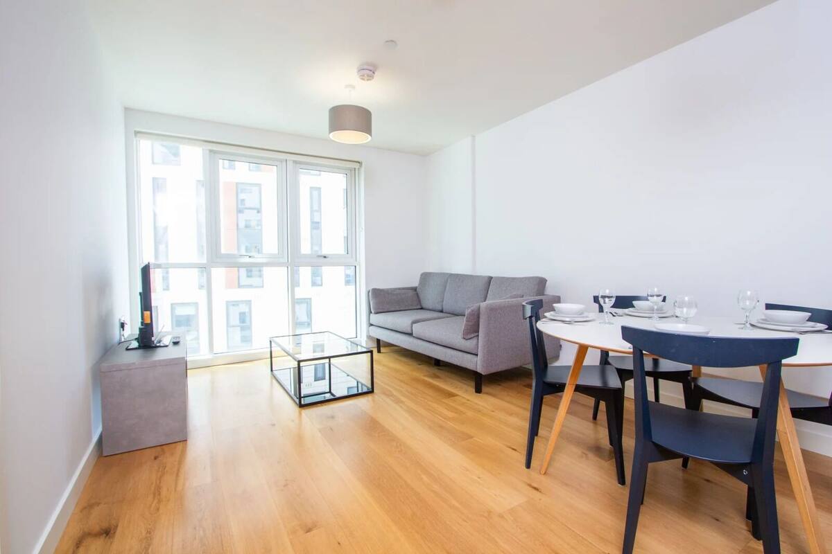 A modern living room with a grey sofa, a glass coffee table, and a dining table set for four.