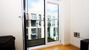 A modern apartment with a large sliding glass door leading to a balcony, wooden flooring, and a visible electrical outlet on the wall. - The Slate Yard (Salford)