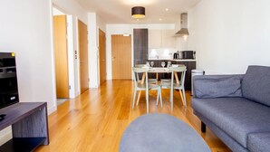 A modern living room with a grey sofa, a dining table with chairs, a TV stand, and a kitchen area with a microwave. - The Slate Yard (Salford)