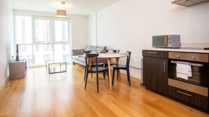 A modern kitchen with dark cabinetry, a microwave, and a small dining table with chairs. - The Slate Yard (Salford)