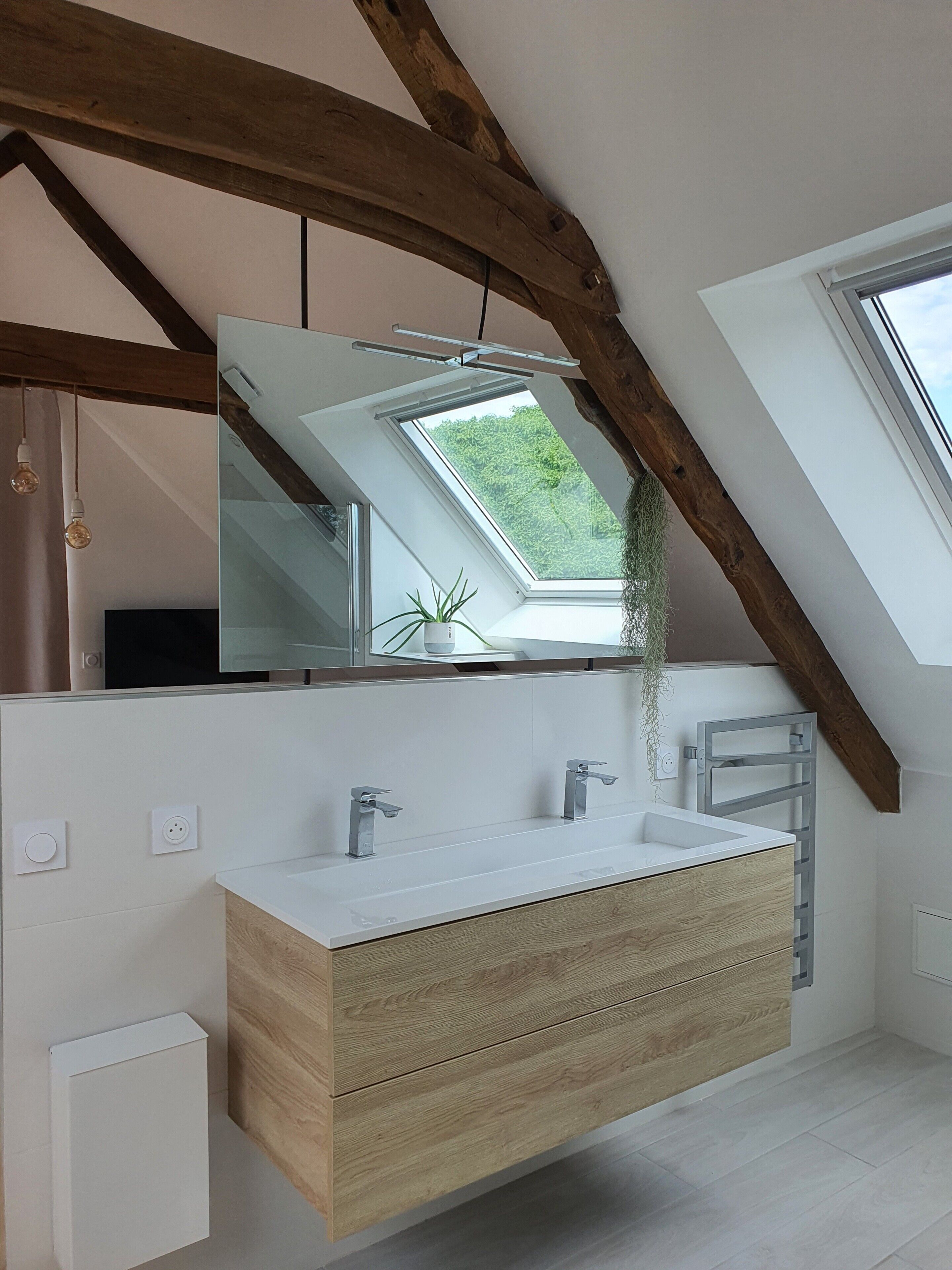 A modern bathroom with a skylight, wooden beams, a large mirror, and a white vanity.