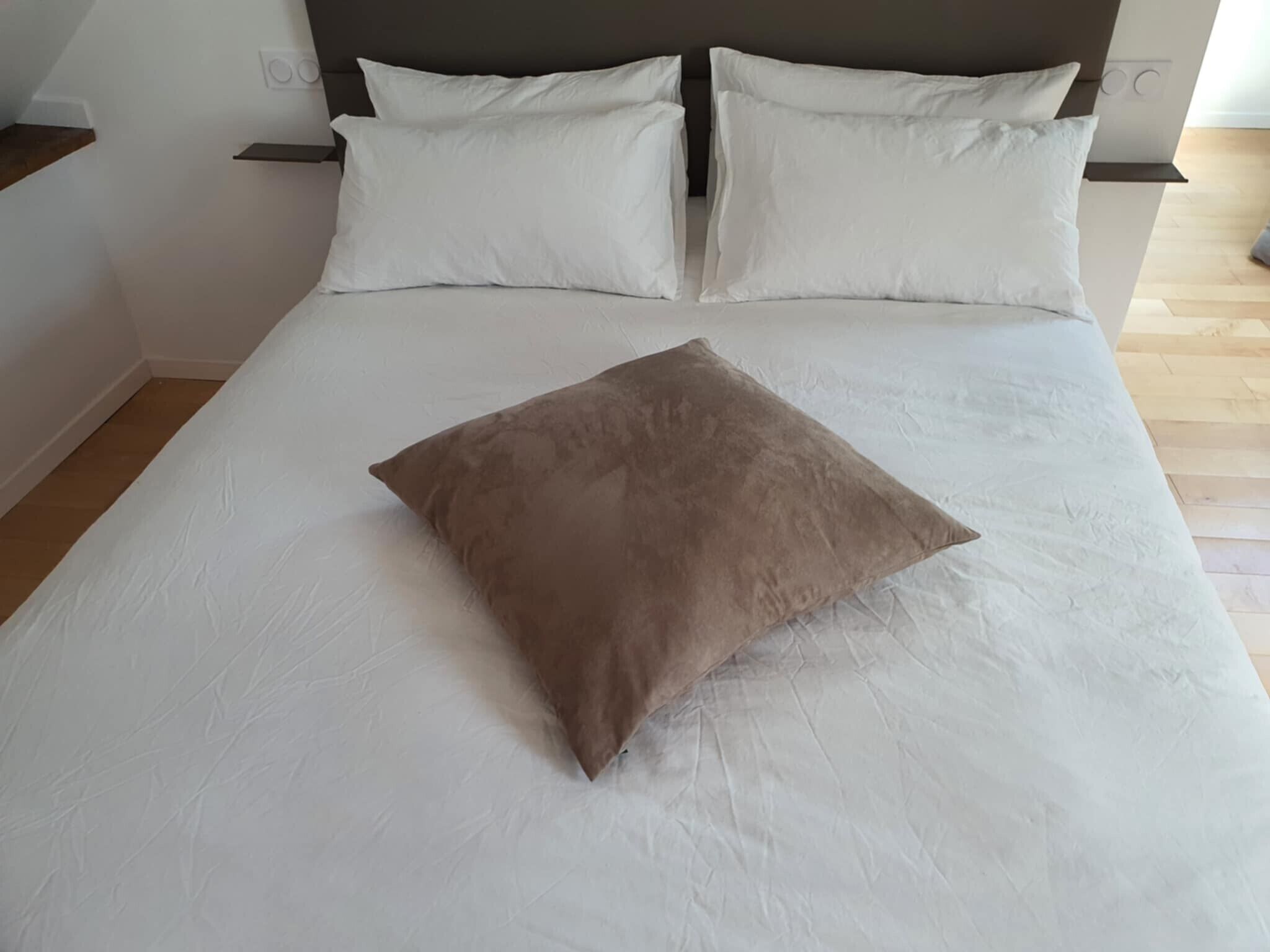 Ein Bett mit weißer Bettwäsche und einem braunen Kopfkissen.