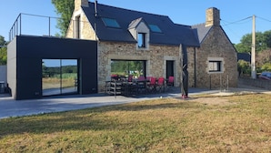 Een stenen huis met een moderne aanbouw, een terras buiten en een helder uitzicht op het omliggende landschap.