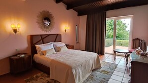 A bedroom with a large bed, two bedside lamps, a decorative mirror, and a view of the outdoors through a sliding door. - Quinta El Molino - Refuge with Swimming Pool in Nature  (Avessada)