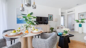 A modern living room with a dining area, featuring a round table, grey upholstered chairs, and a flat-screen TV. - Versilian Tuscan coast escape (Viareggio)