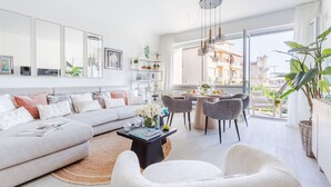 A modern living room with a sofa, chairs, a coffee table, and a dining area with a table and chairs. There are large windows providing a view of the outside. - Versilian Tuscan coast escape (Viareggio)
