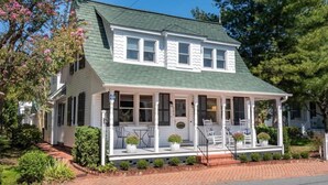 A two-story house with a green roof, white exterior, and a porch with white railings and potted plants. - The Snuggery Inn & Suites Captain`s Quarters (Saint Michaels)