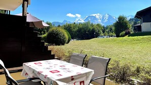 Un espace extérieur aménagé avec une table et des chaises, un banc abrité et une vue sur des montagnes enneigées.