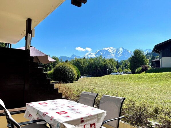 An outdoor seating area with a table and chairs, a covered bench, and a view of snow-capped mountains.