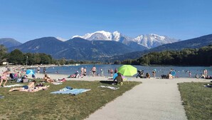 Une plage au bord d’un lac, où des gens se prélassent au soleil et se baignent, le tout entouré de montagnes.
