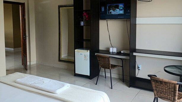 Habitación de hotel con cama, escritorio con silla, refrigerador pequeño, televisor montado en la pared y perchero.