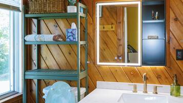 Une salle de bain aux murs lambrissés, équipée de toilettes, d’un lavabo avec un miroir au-dessus et d’une étagère contenant des articles de toilette.