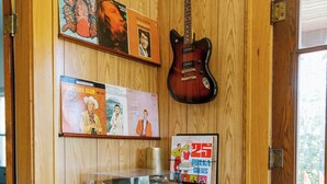Ein Zimmer mit Holzwänden, einer Holztür, einem schwarz-weißen Schrank, einer Gitarre und gerahmten Postern.