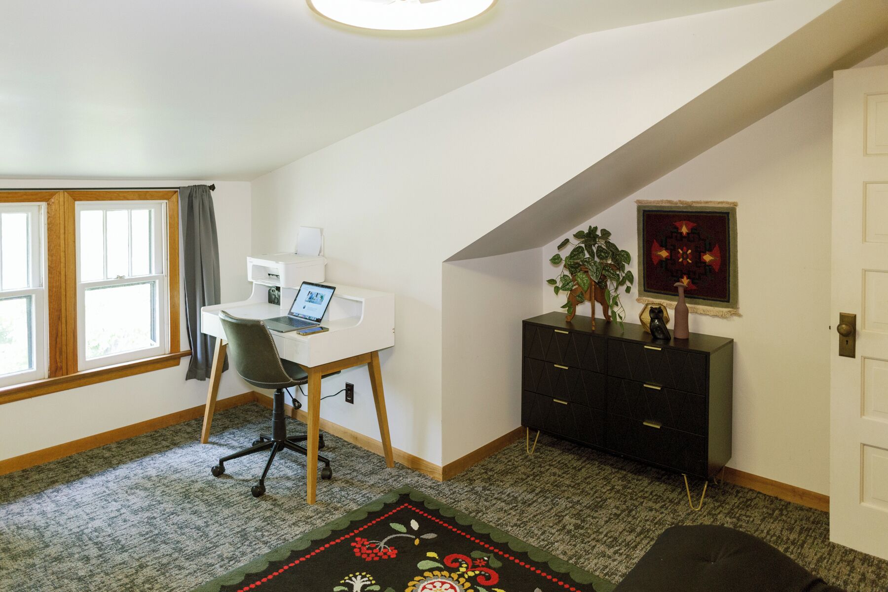 Een kamer met een bureau, stoel en een zwarte kast met decoratieve spullen.