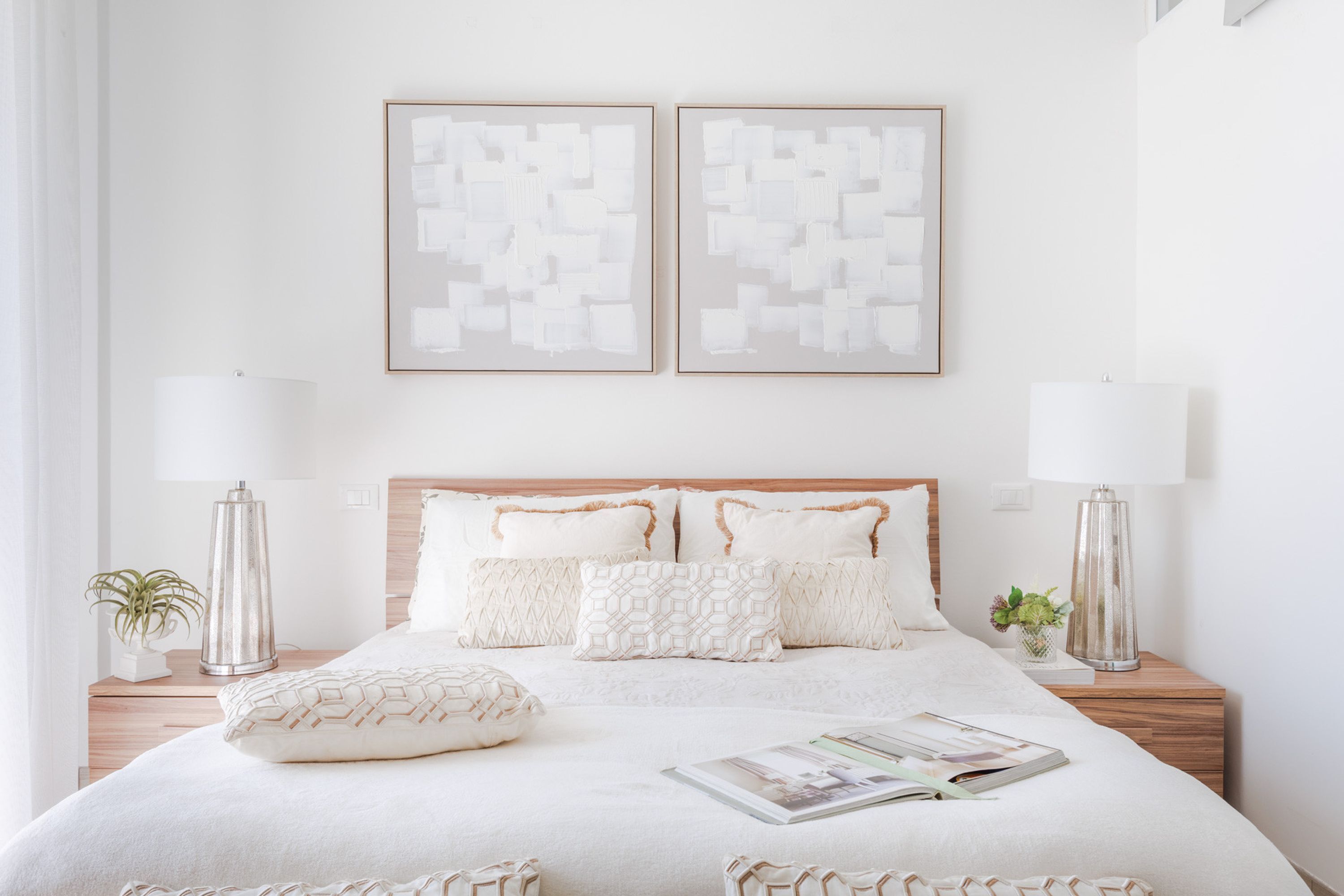 Een keurig opgemaakt slaapkamer met een houten hoofdeinde, twee nachtkastjes met lampen, een bed met gestreepte kussens en twee ingelijste abstracte kunstwerken aan de muur.