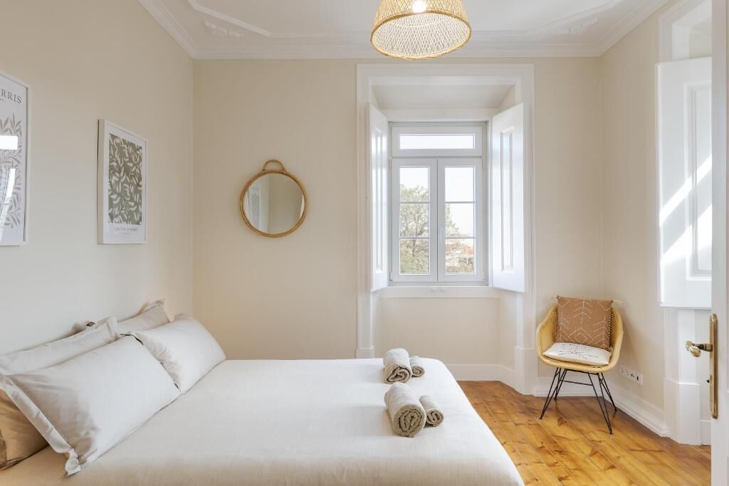 A bedroom with a large bed, a window, a chair, and a mirror.
