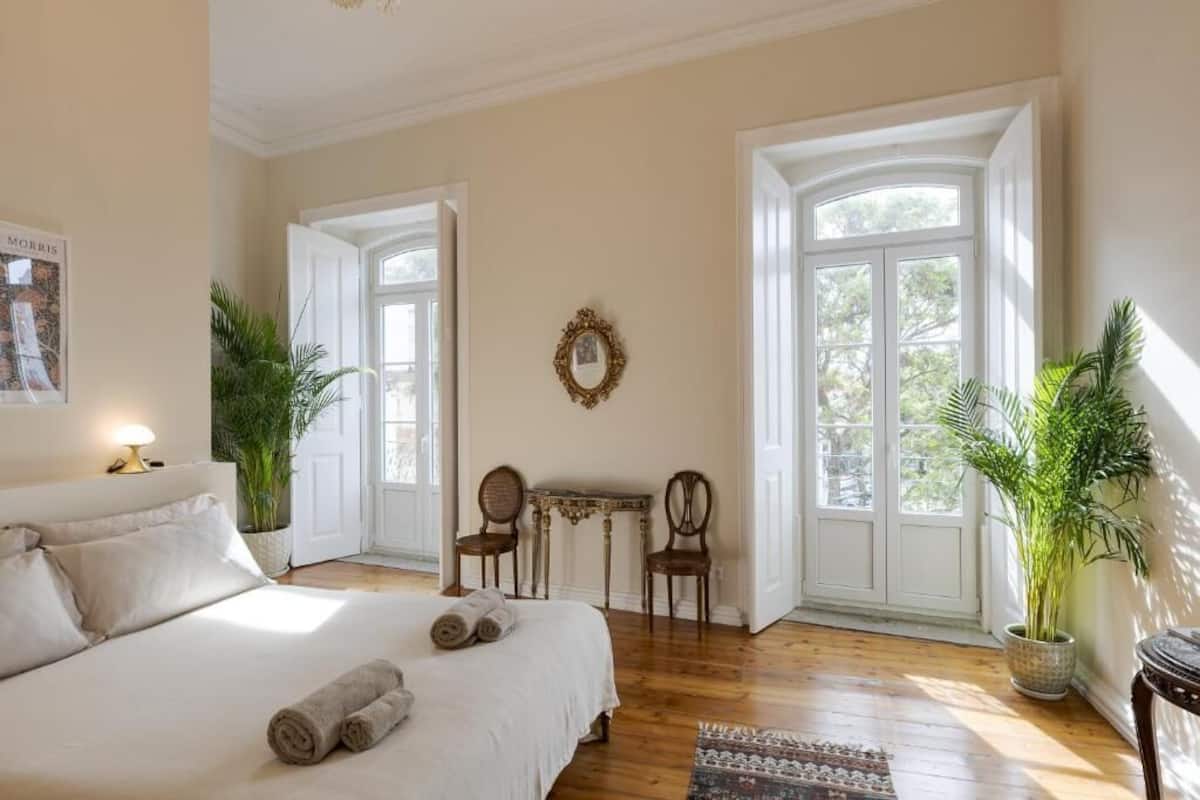 Un dormitorio con una cama grande, dos sillas, una mesita y un espejo en la pared.