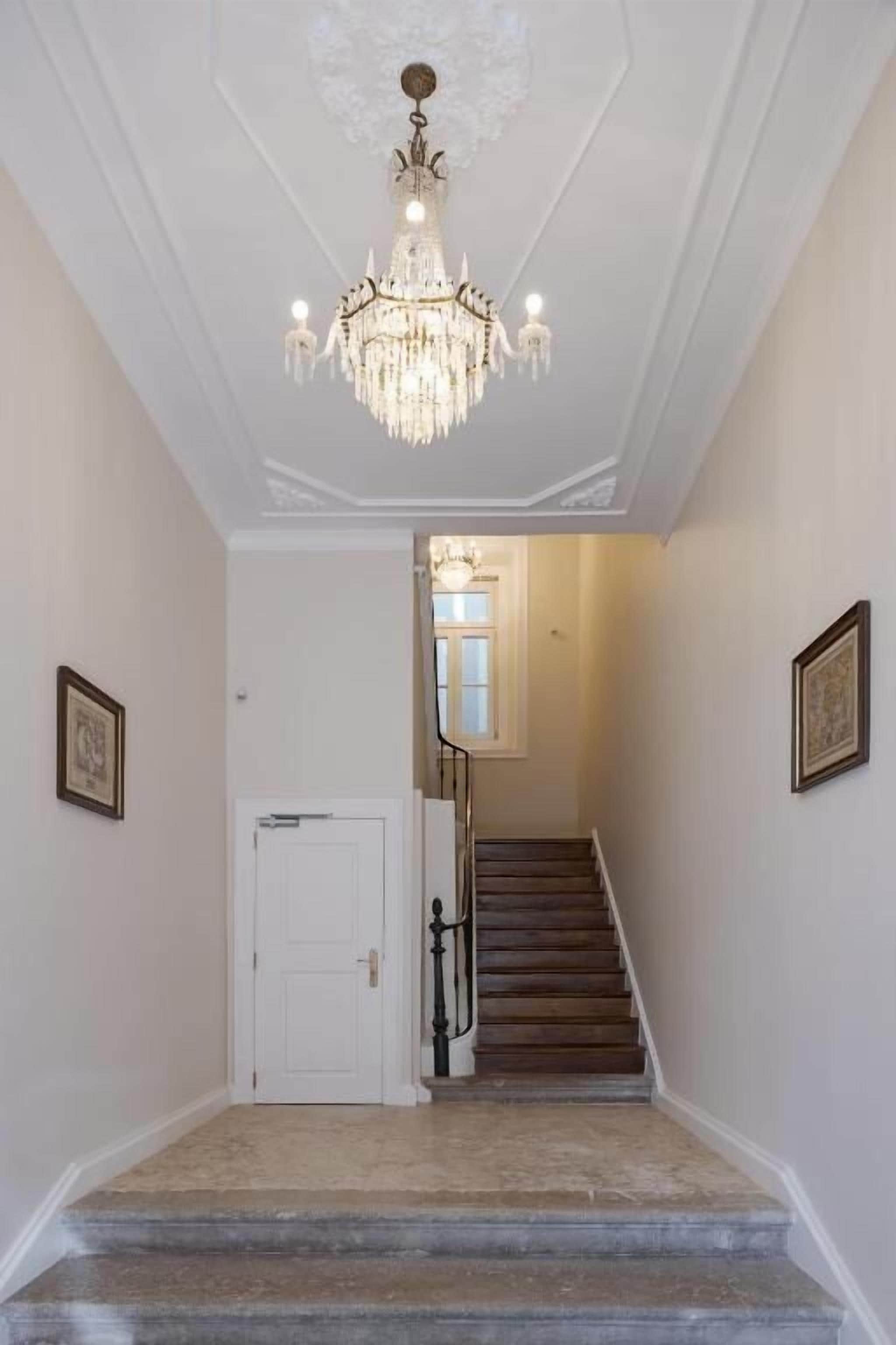 A grand staircase with a chandelier, white walls, and framed pictures.