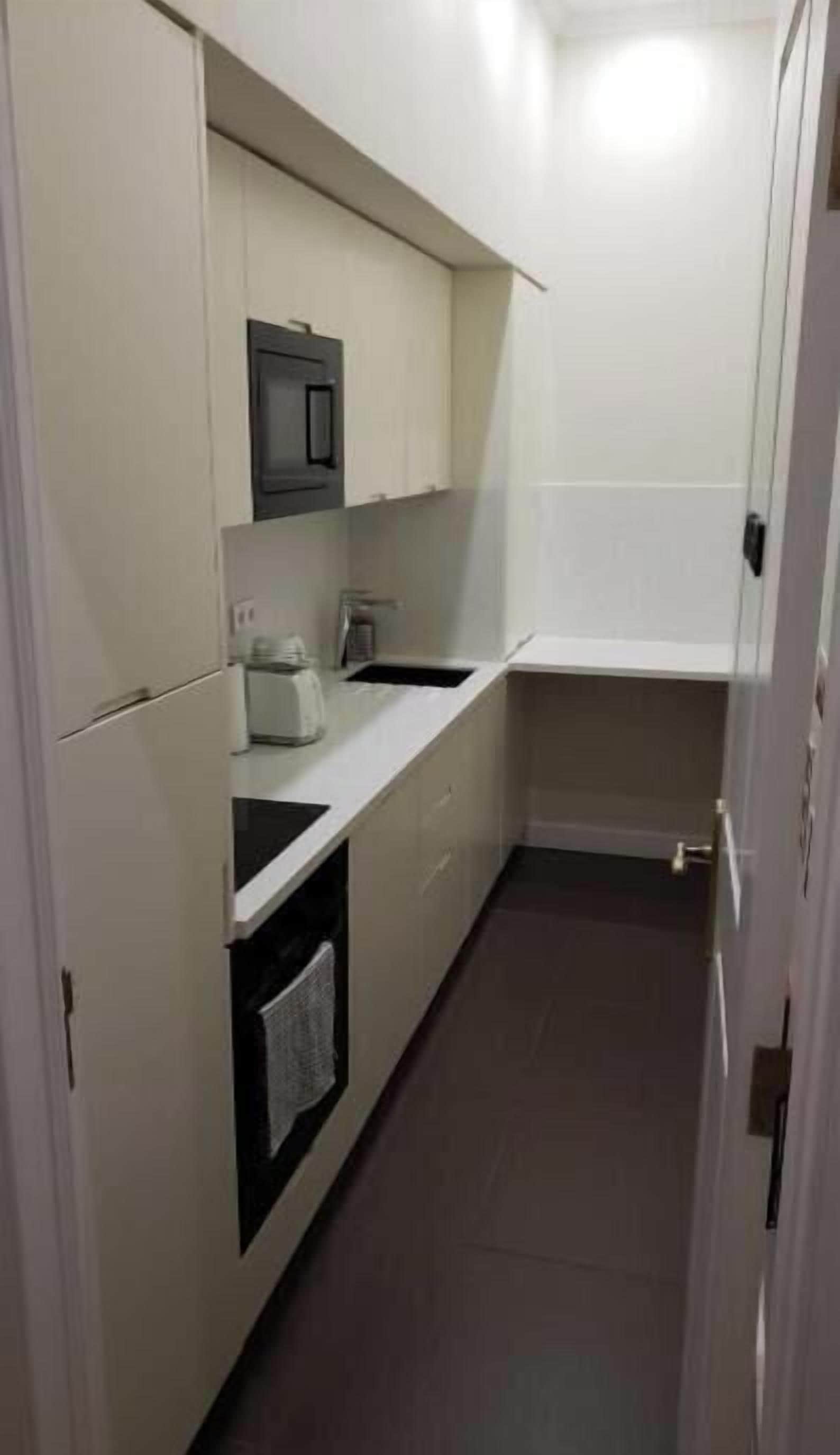A narrow kitchen with white cabinets, a microwave, a kettle, and a sink.