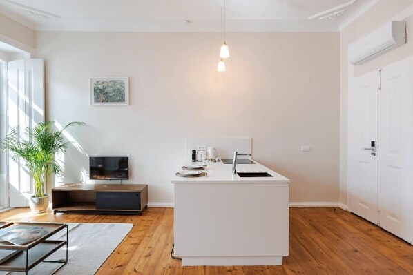 Una cocina moderna con una isla blanca, suelo de madera, un televisor de pantalla plana y una planta en maceta.