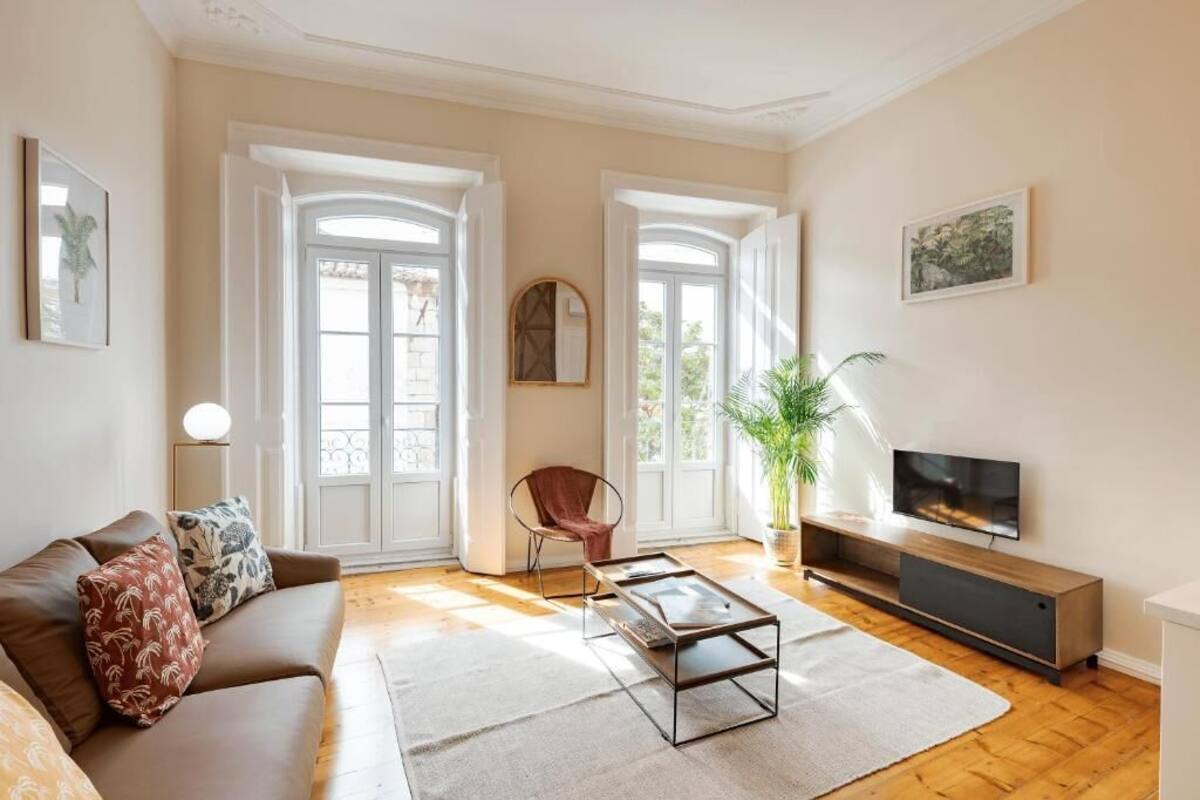 Una sala de estar con sofá, mesa de centro, televisor y ventanas amplias.