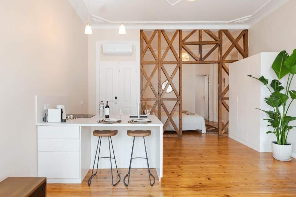 Una cocina moderna con encimera blanca, dos taburetes y vigas de madera al fondo.
