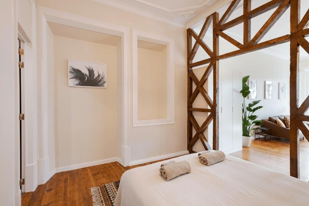 A bedroom with a wooden partition, a bed with rolled towels, a wall-mounted artwork, and a potted plant.