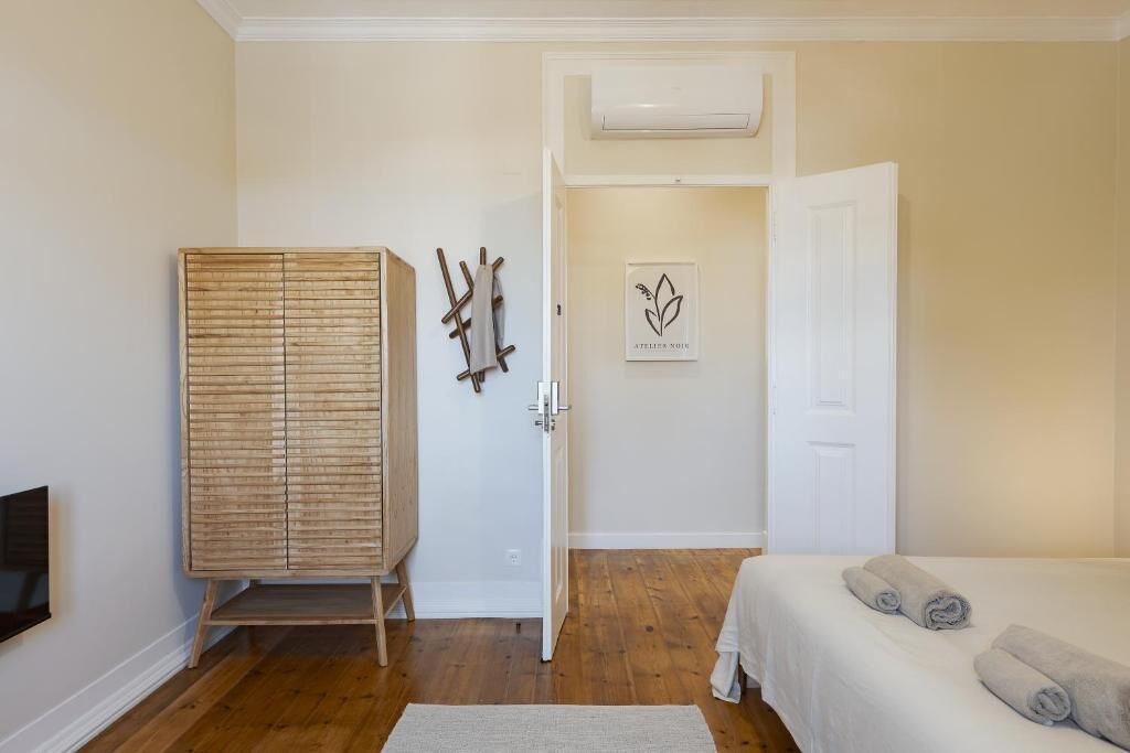 Ein Schlafzimmer mit einem Holzschrank, einem Bett mit aufgerollten Handtüchern, einer weißen Tür und einer Wand-Klimaanlage.