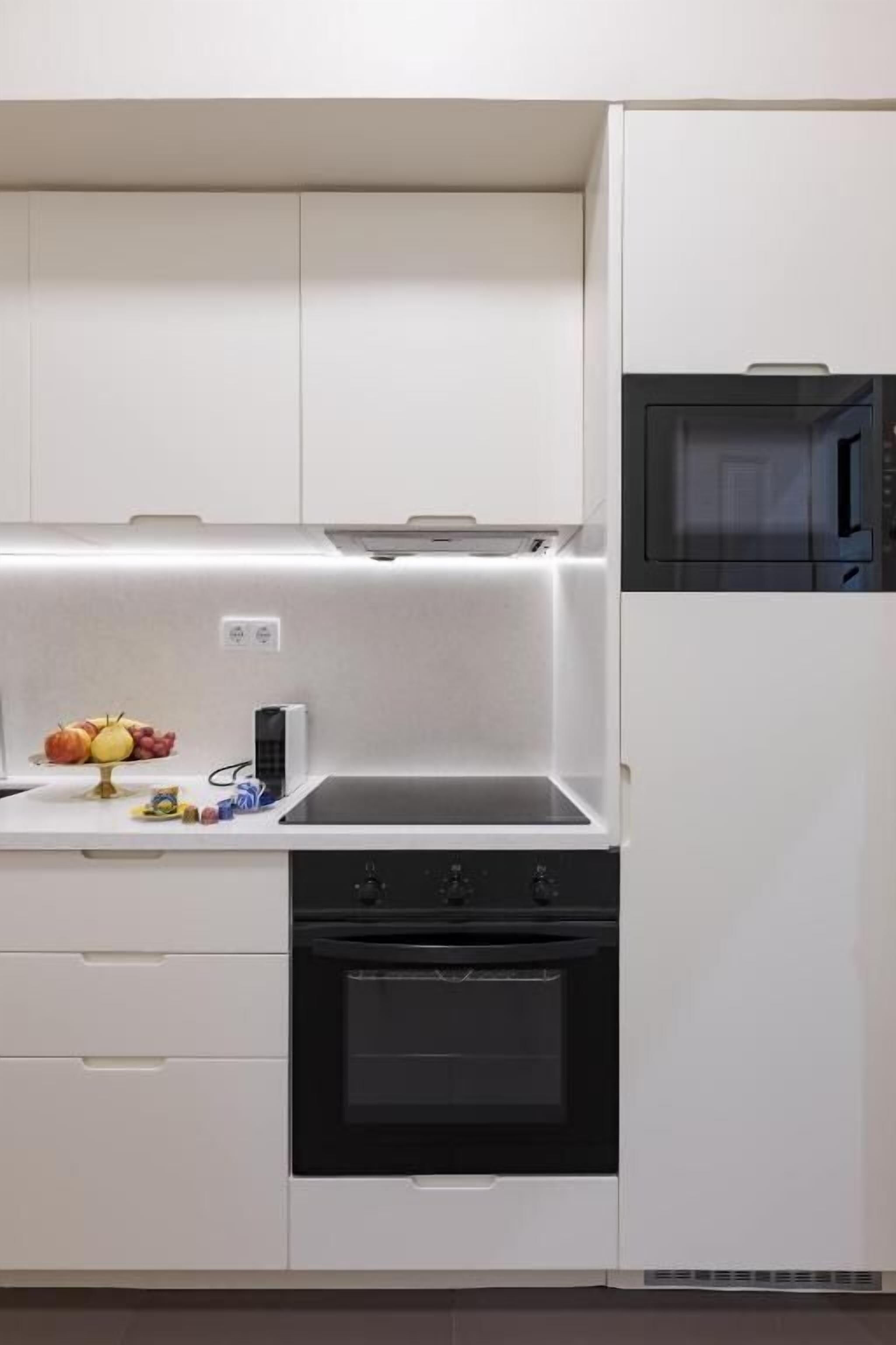A compact kitchen with white cabinets, a black oven, and a microwave.