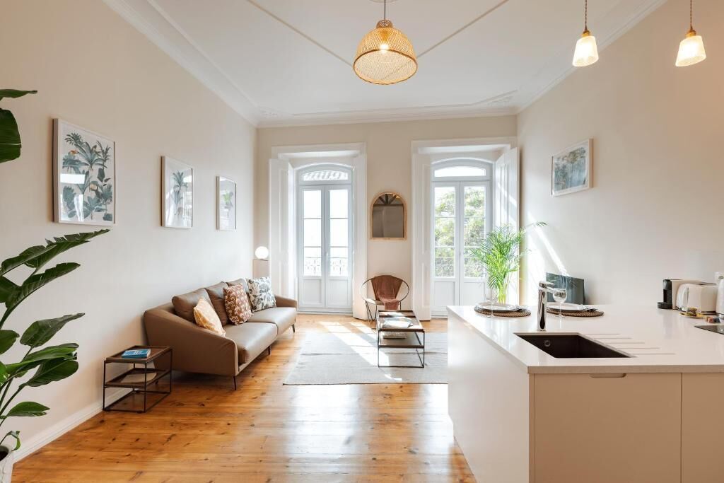 Ett modernt vardagsrum med en soffa, ett soffbord och en matplats. Det finns stora fönster, en kristallkrona och konstverk på väggarna.
