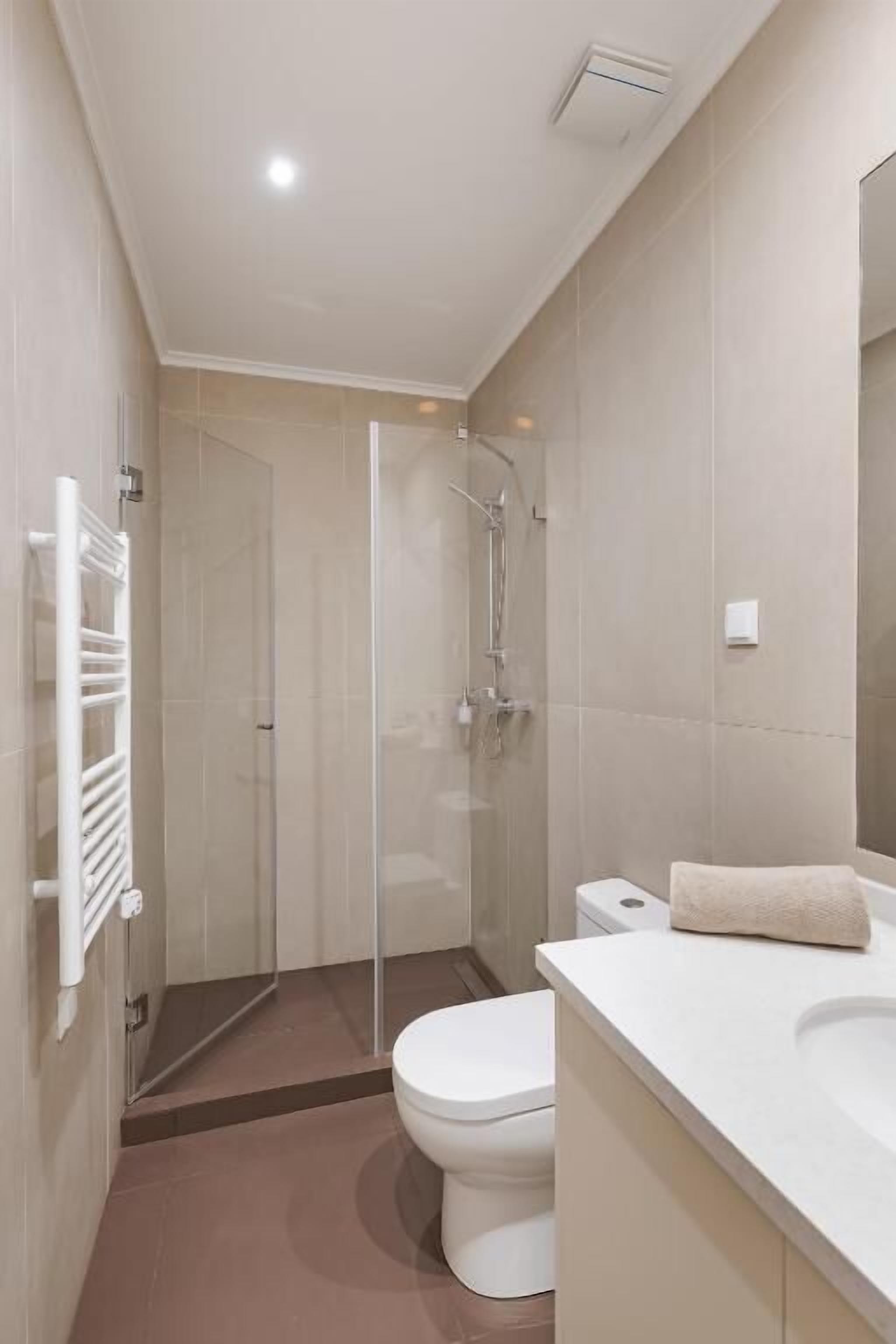 A modern bathroom with a glass-enclosed shower, a white toilet, and a white sink with a towel on the counter.