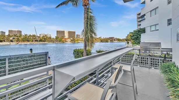 Ein Balkon mit Blick auf einen Fluss, Palmen und moderne Gebäude im Hintergrund.