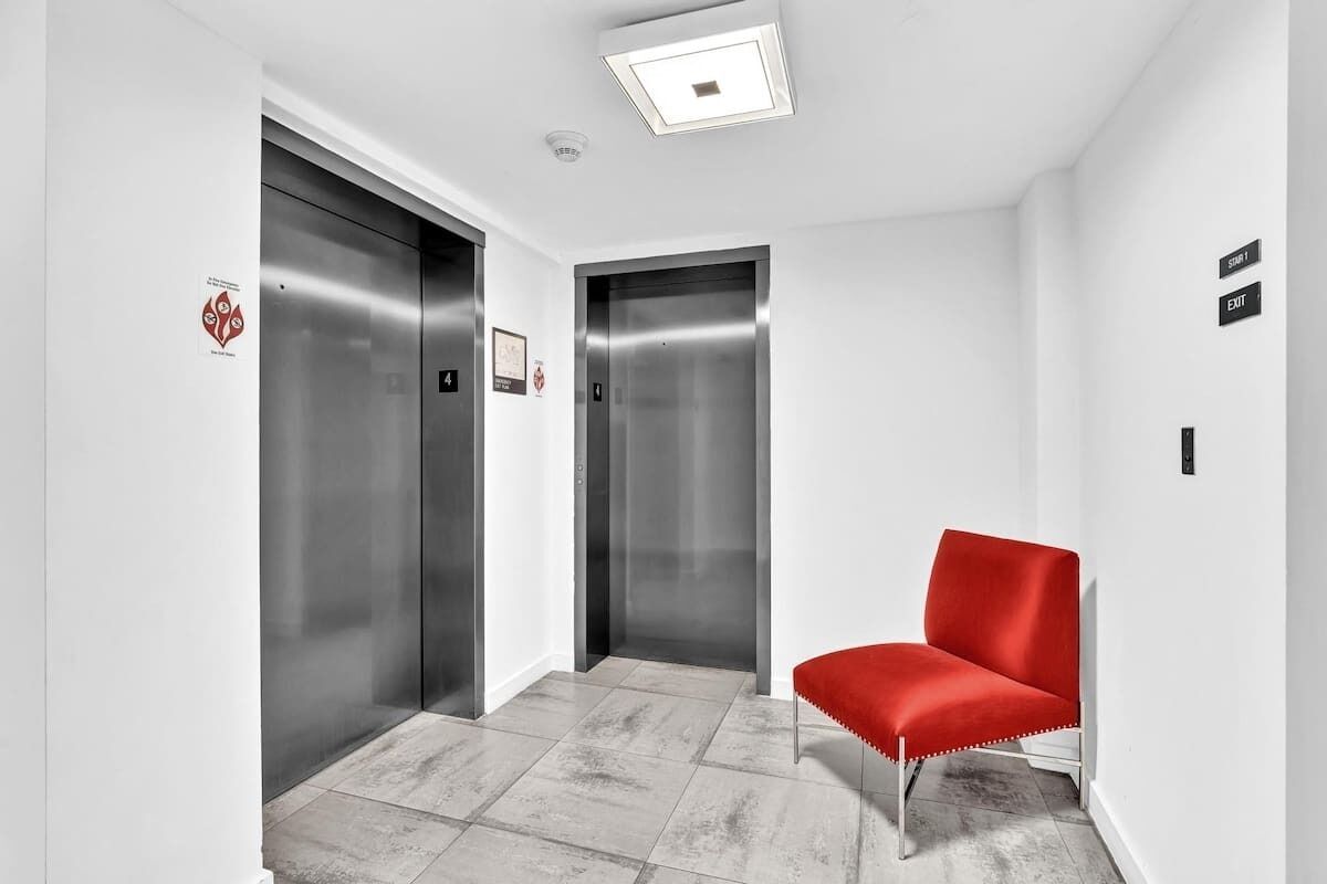 A modern elevator area with two elevators, a red chair, and a clean, white interior.