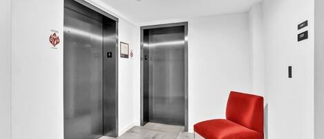 A modern elevator area with two elevators, a red chair, and a clean, white interior.