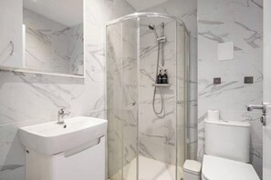 A modern bathroom with a glass-enclosed shower, a white sink, and a toilet.
