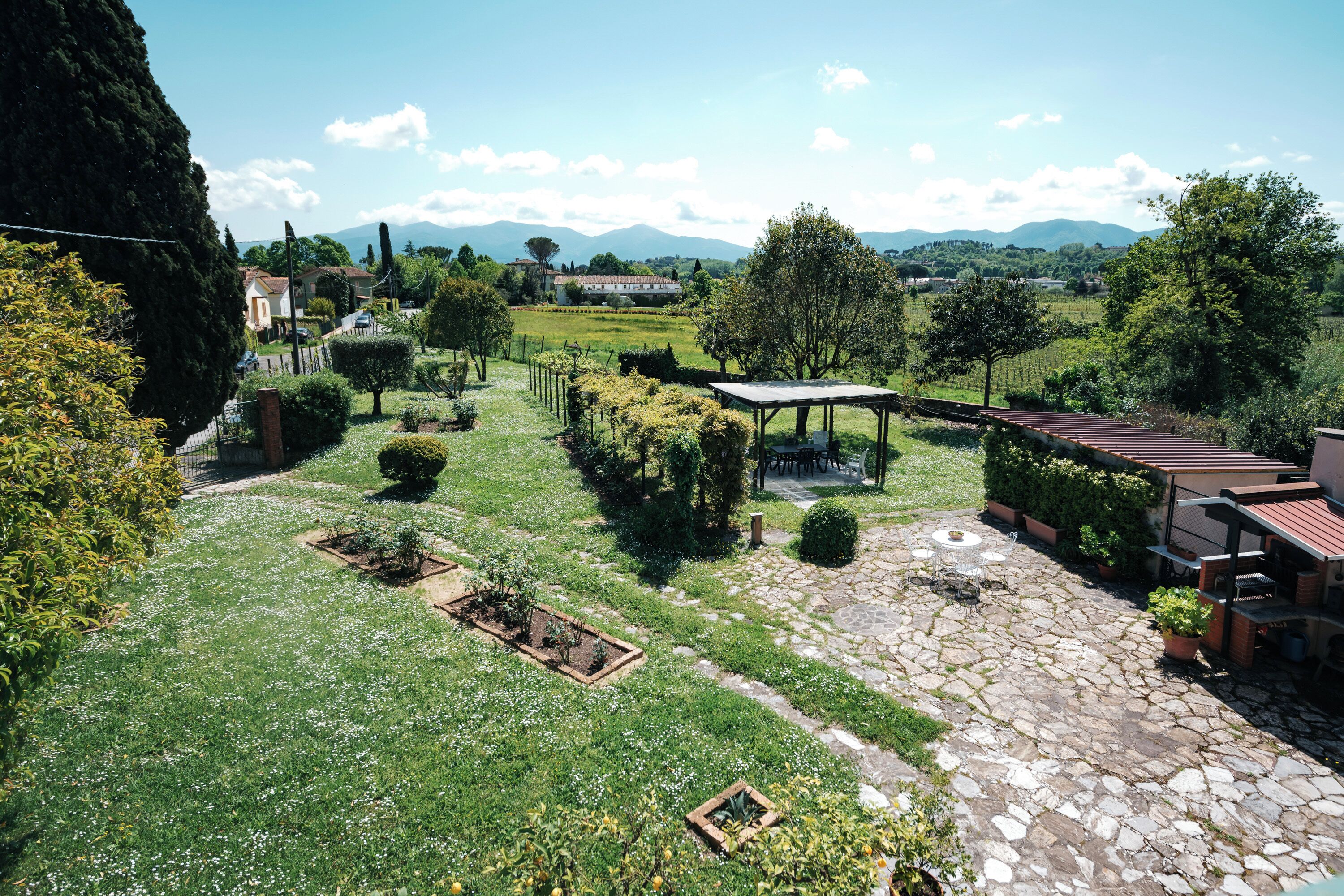 Un jardin agrémenté d’une terrasse en pierre, d’une pergola et offrant une vue sur des collines lointaines.