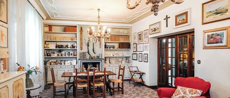 A room with a dining table, chairs, a red armchair, a chandelier, and a bookshelf filled with books and decorative items.
