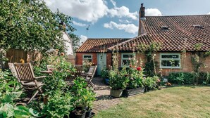 A brick house with a tiled roof, a garden with potted plants, and wooden furniture.