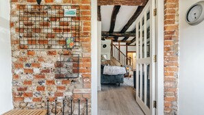 A narrow hallway with exposed brick walls, a wooden bench, and a door leading to a room with a bed and a lamp.