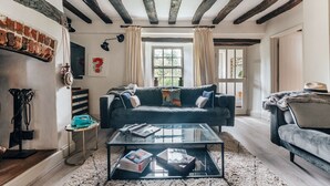 A cozy living room with a dark blue sofa, a glass coffee table with books, a brick wall, and a window with curtains.
