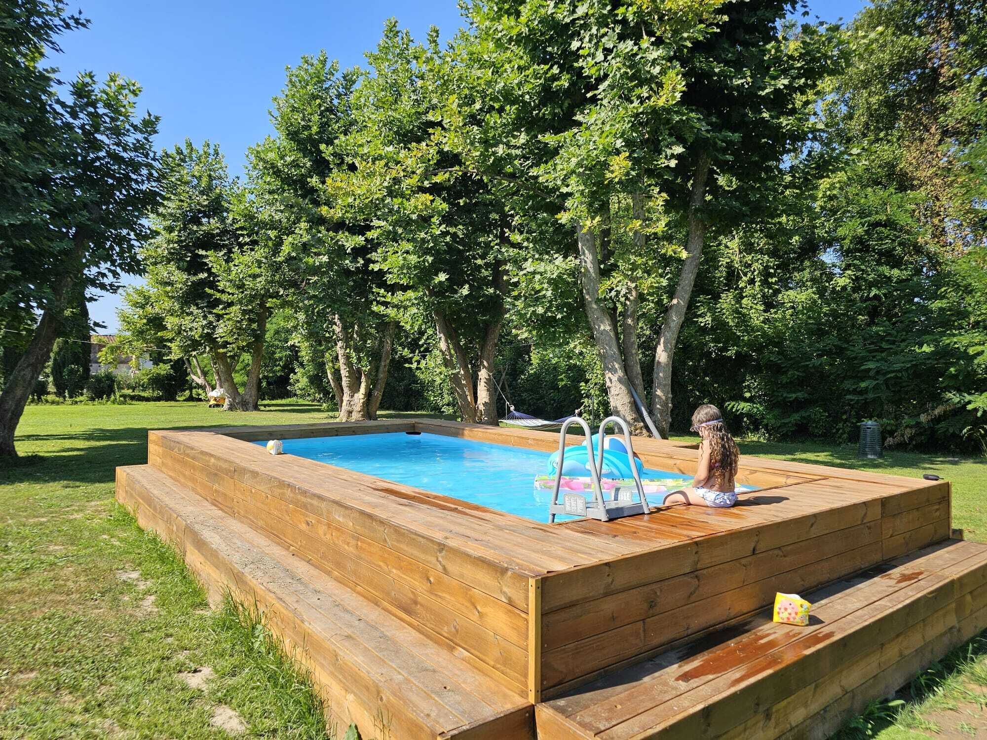 Une terrasse en bois avec une piscine, entourée d’arbres et d’herbe.
