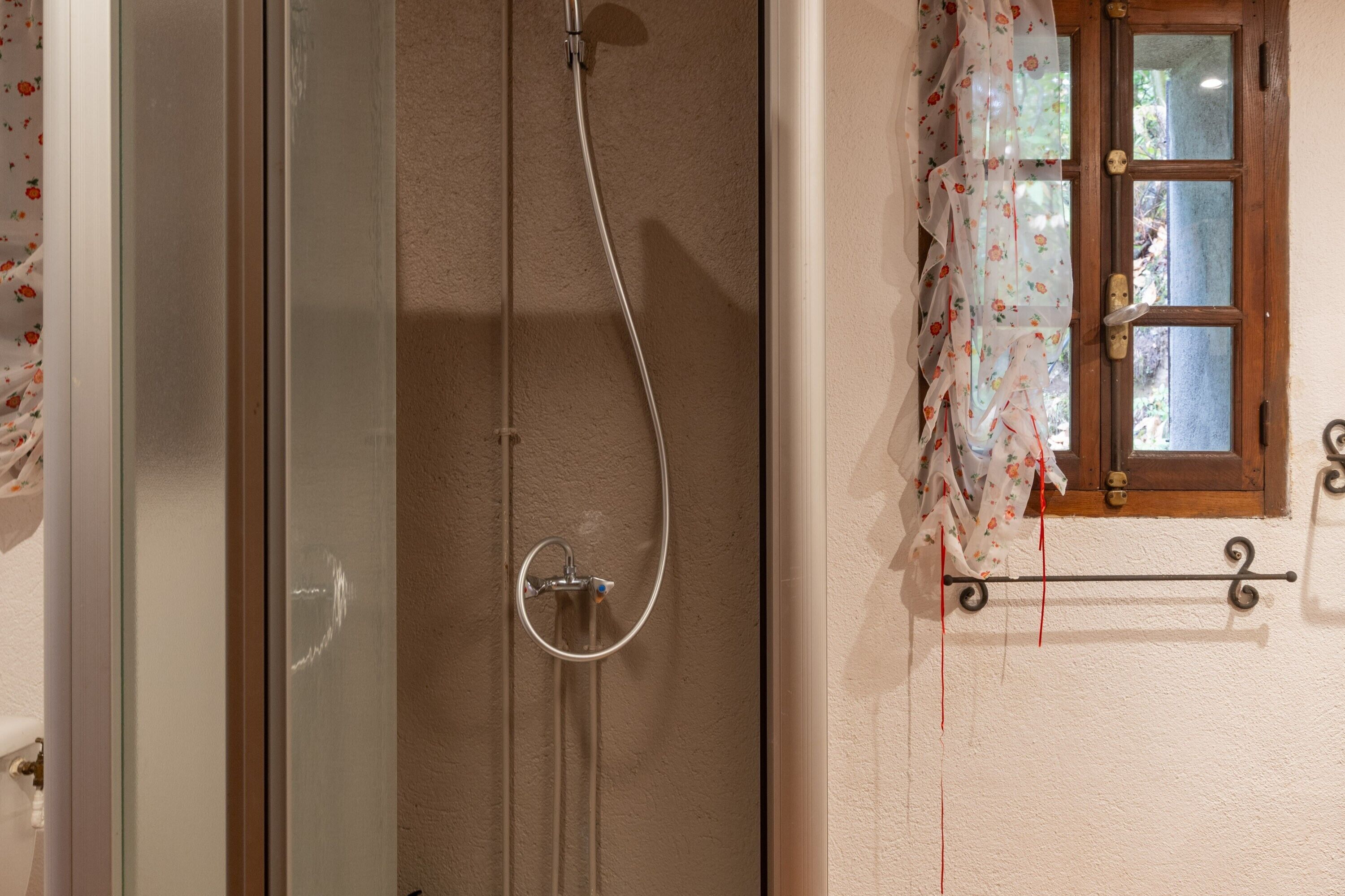 Une salle de bain avec une douche à parois de verre, une porte en bois et une fenêtre ornée de rideaux à motifs floraux.